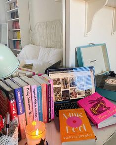 there are many books on the table next to a laptop and a candle in front of it