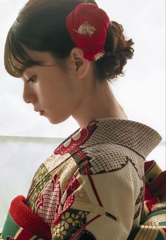 a woman with a red flower in her hair wearing a kimono and looking out the window