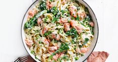 a pan filled with pasta and vegetables on top of a white table next to utensils