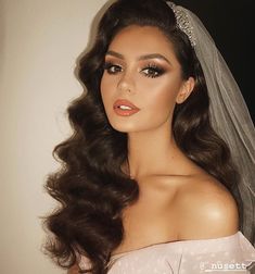 a woman with long hair wearing a bridal veil and makeup on her wedding day