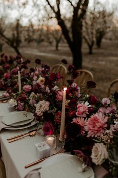 a long table with flowers and candles on it is set for an outdoor dinner party