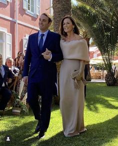 a man and woman in formal wear walking on the grass with palm trees behind them