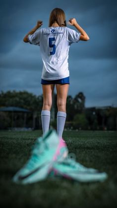 a female soccer player standing in the grass with her back to the camera and holding her hands behind her head