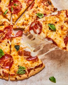 a pizza with pepperoni and basil on it is cut into slices, sitting on a piece of parchment paper