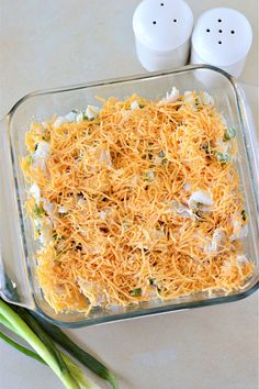 a casserole dish with cheese and green onions on the side next to two salt shakers