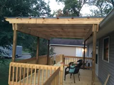 a covered patio with chairs and table on the back deck in front of a house