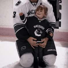 a young boy sitting on the ice with an older man in hockey uniform behind him