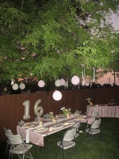 a table set up for an outdoor party with balloons and lights hanging from the tree