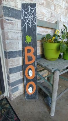 a wooden sign that says boo on it next to a potted plant and chair