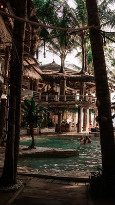 the pool is surrounded by palm trees and thatched umbrellas, with people swimming in it