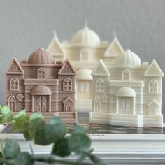 three small buildings sitting on top of a table next to green plants and flowers in front of them