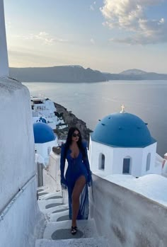 a woman in a blue dress is standing on some steps by the water and looking at the camera