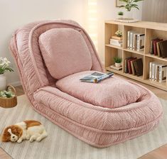 a cat laying on the floor next to a pink chair with a book in it