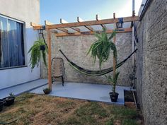 a hammock hanging from the side of a house next to a yard with potted plants