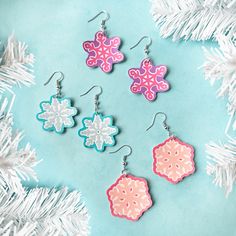 four snowflake earrings are hanging from a white christmas tree ornament on a blue background