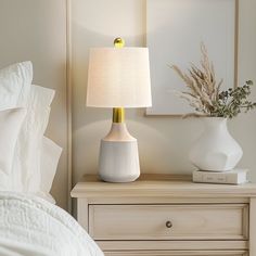 a white lamp sitting on top of a wooden dresser next to a night stand with flowers