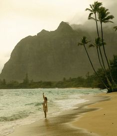 a woman standing on top of a sandy beach next to the ocean