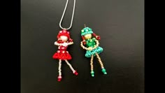 two beaded doll pendants on a black surface, one is red and the other is green