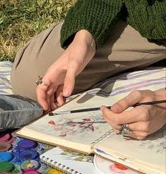 a person sitting on the ground with an open book and pen in their hand while writing