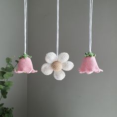 three crocheted flowers hanging from strings next to a potted plant in a room