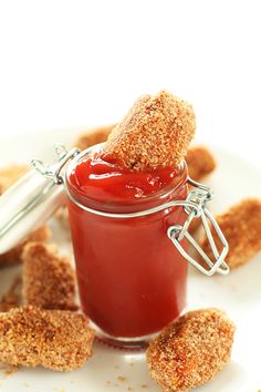 a jar filled with ketchup sitting on top of a white plate next to small pieces of bread