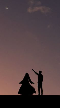 two people standing on top of a hill under a cloudy sky with the moon in the distance