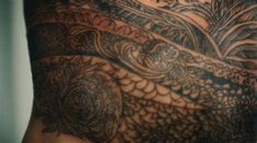 the back of a man's body with tattoos on his arm and chest,