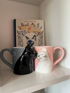 two coffee mugs sitting on top of a white shelf next to a bookcase