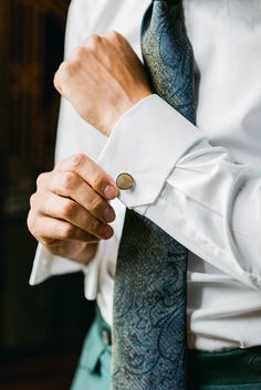 a man wearing a white shirt and blue tie adjusting his cufflinks with one hand