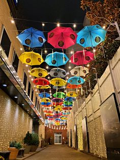 many colorful umbrellas hanging from the ceiling in an alleyway at night with lights