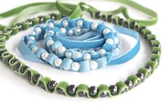 three pieces of blue and green beaded necklaces on a white surface with ribbon