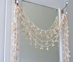 a mirror with pearls hanging from it's side next to a wall mounted mirror