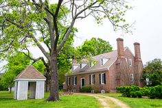 an old brick house in the middle of a green field with trees and bushes around it