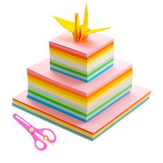 a stack of multicolored paper with scissors next to it on a white background