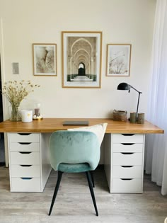 an office desk with two pictures on the wall and a chair in front of it