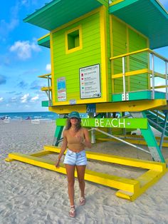 a woman standing in front of a yellow and green lifeguard tower on the beach