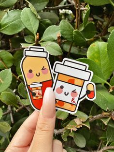 a hand holding up a sticker with two coffee cups on it, and the other one is in front of some leaves