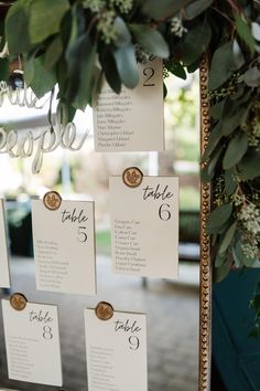 seating cards are attached to a gold frame with greenery and flowers on the table