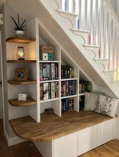 a bookshelf under the stairs in a house with wooden floors and white walls