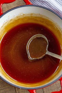 a spoon in a bowl filled with sauce on top of a wooden table next to a red and white towel