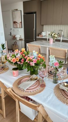 the table is set with pink and yellow flowers in glass vases, gold plates, and silverware