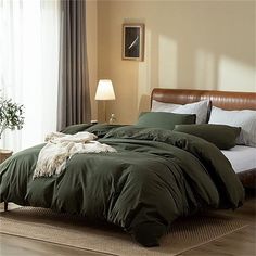 a bed with green comforter and pillows in a room next to a lamp on a table