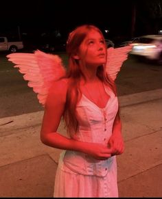 a woman with angel wings standing on the side of a road at night, looking up to the sky