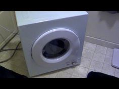 a white washing machine sitting on top of a bathroom floor next to a toilet paper dispenser