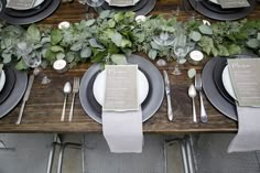 the table is set with black and white plates, silverware, greenery and candles