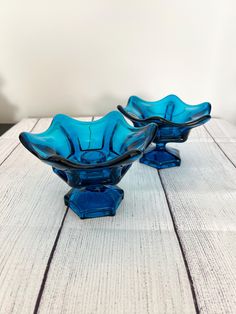 two blue glass bowls sitting on top of a white wooden table next to each other