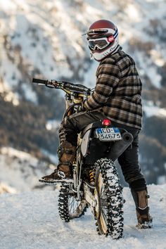 a man riding on the back of a dirt bike down a snow covered slope with mountains in the background