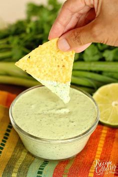 a hand dipping a tortilla chip into a bowl of dip with asparagus and cilantro in the background