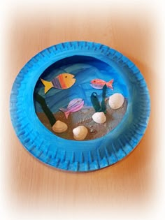 a paper plate that has some fish in it on the table with sand and water