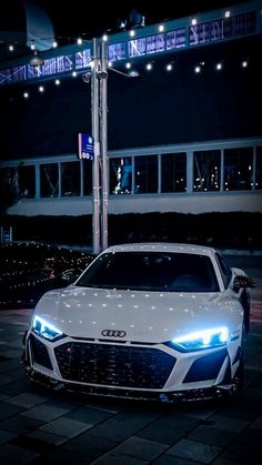 a white sports car parked in front of a building with lights on it's sides